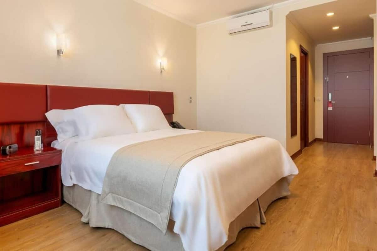 Een hotelkamer met een bed, nachtkastje, telefoon en een wandairconditioner.