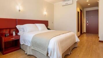 Una habitación de hotel con una cama, una mesita de noche, un teléfono y un aire acondicionado instalado en la pared.