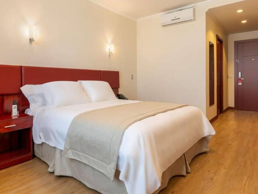Una habitación de hotel con una cama, una mesita de noche, un teléfono y un aire acondicionado instalado en la pared.