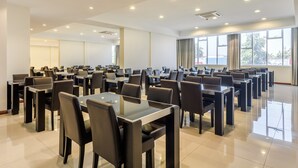 Una amplia sala de conferencias con varias mesas y sillas, ventanas grandes y luces de techo.