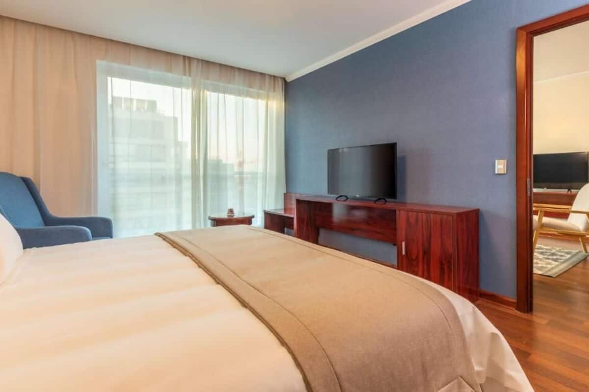 Hotelkamer met een groot bed, een televisie op een houten standaard, een stoel en uitzicht op de stad.
