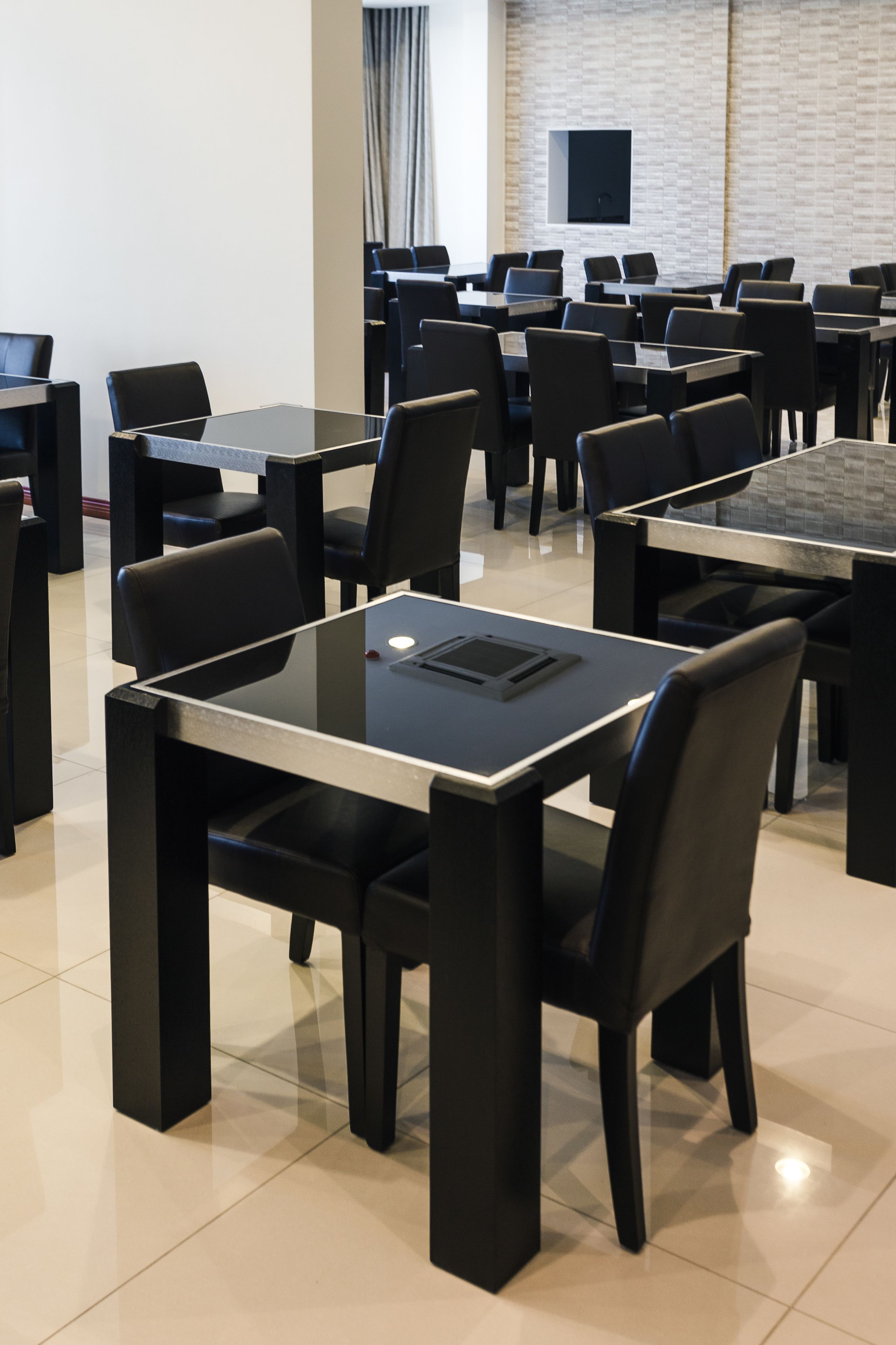 A conference room with multiple tables and chairs, a flat-screen TV mounted on the wall, and a tiled floor.
