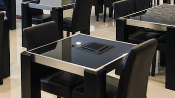 A conference room with multiple tables and chairs, a flat-screen TV mounted on the wall, and a tiled floor.