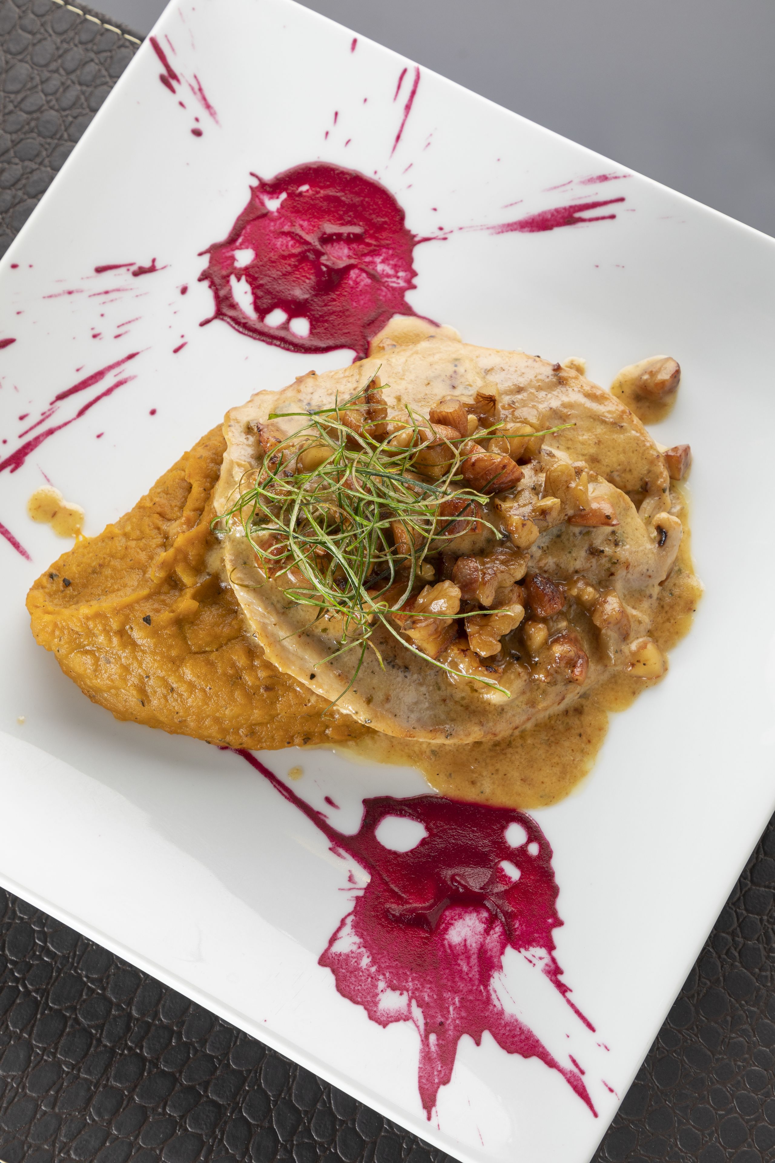 Une assiette carrée contenant un plat, une sauce avec des éclaboussures rouges, et une surface texturée en dessous.