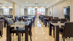 Un comedor moderno con varias mesas y sillas, ventanas grandes y una pared de ladrillo.