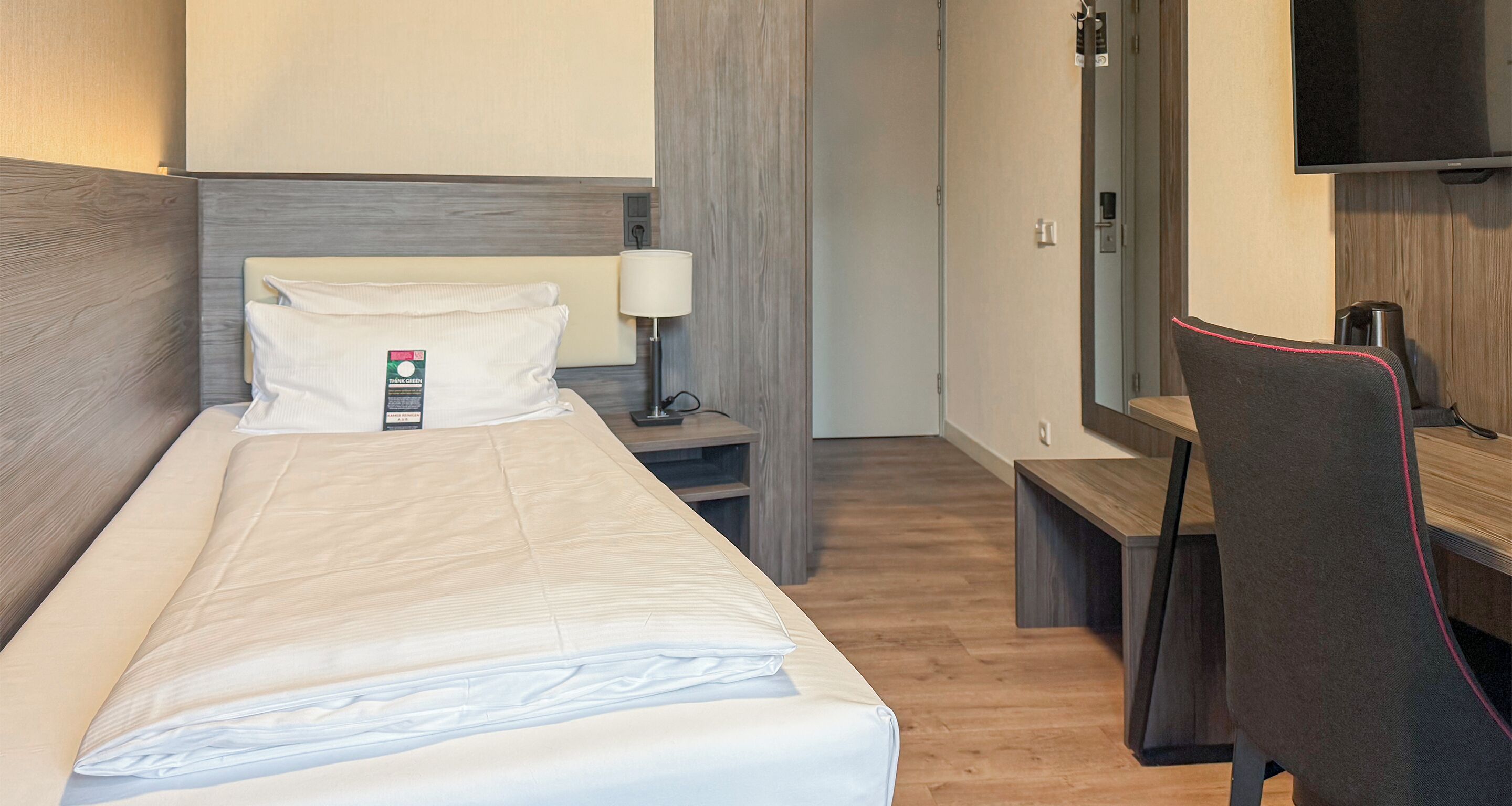 A hotel room with a bed, a desk, a chair, a TV, and a nightstand.