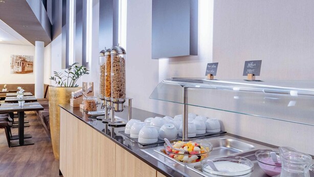Un área de bufé con diversas opciones de comida, que incluye una estación de ensaladas de frutas, yogur y un dispensador de zumos.