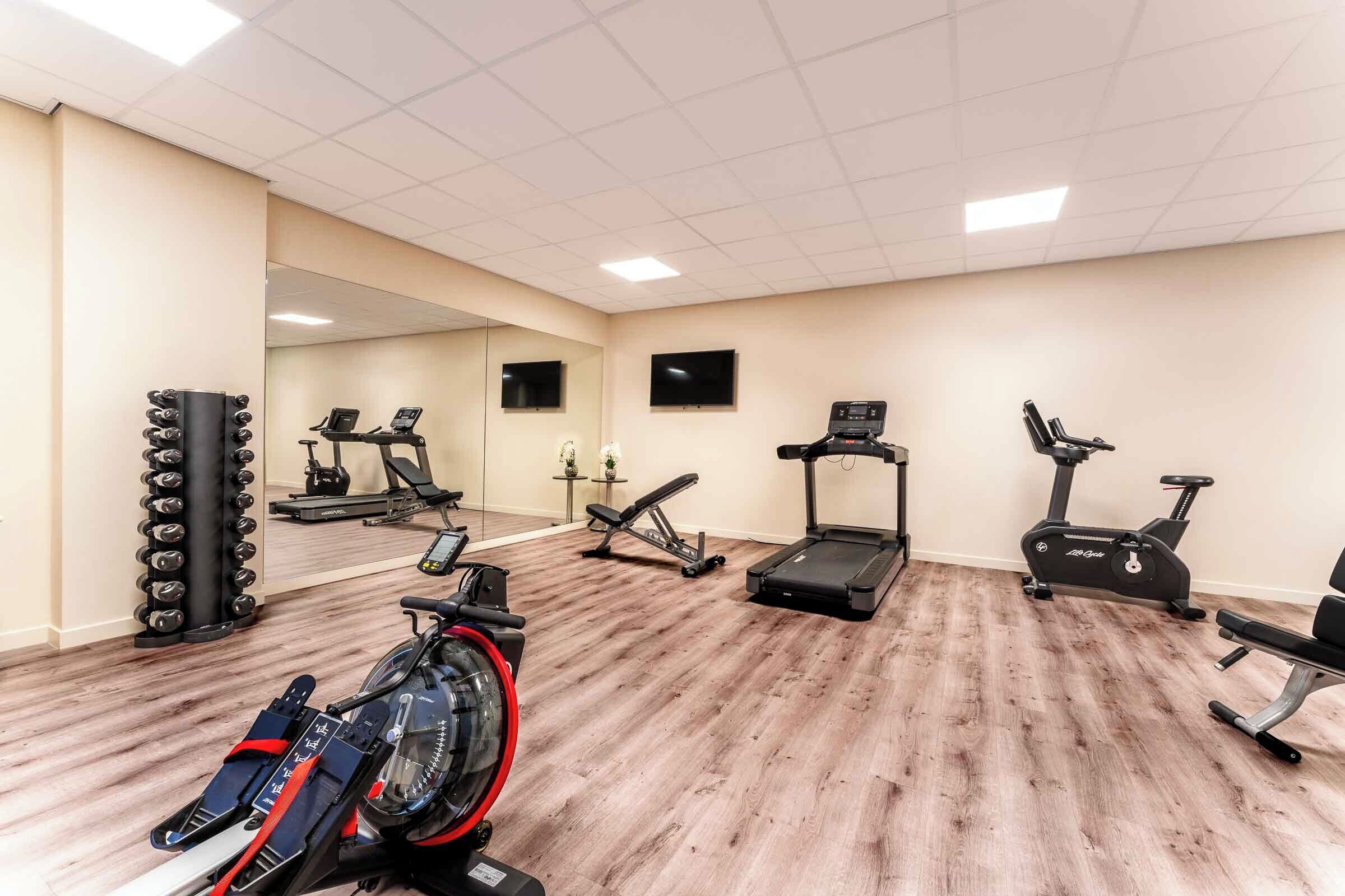 Ein Fitnessraum mit Trainingsgeräten, darunter ein Laufband, ein Crosstrainer und ein Ergometer.