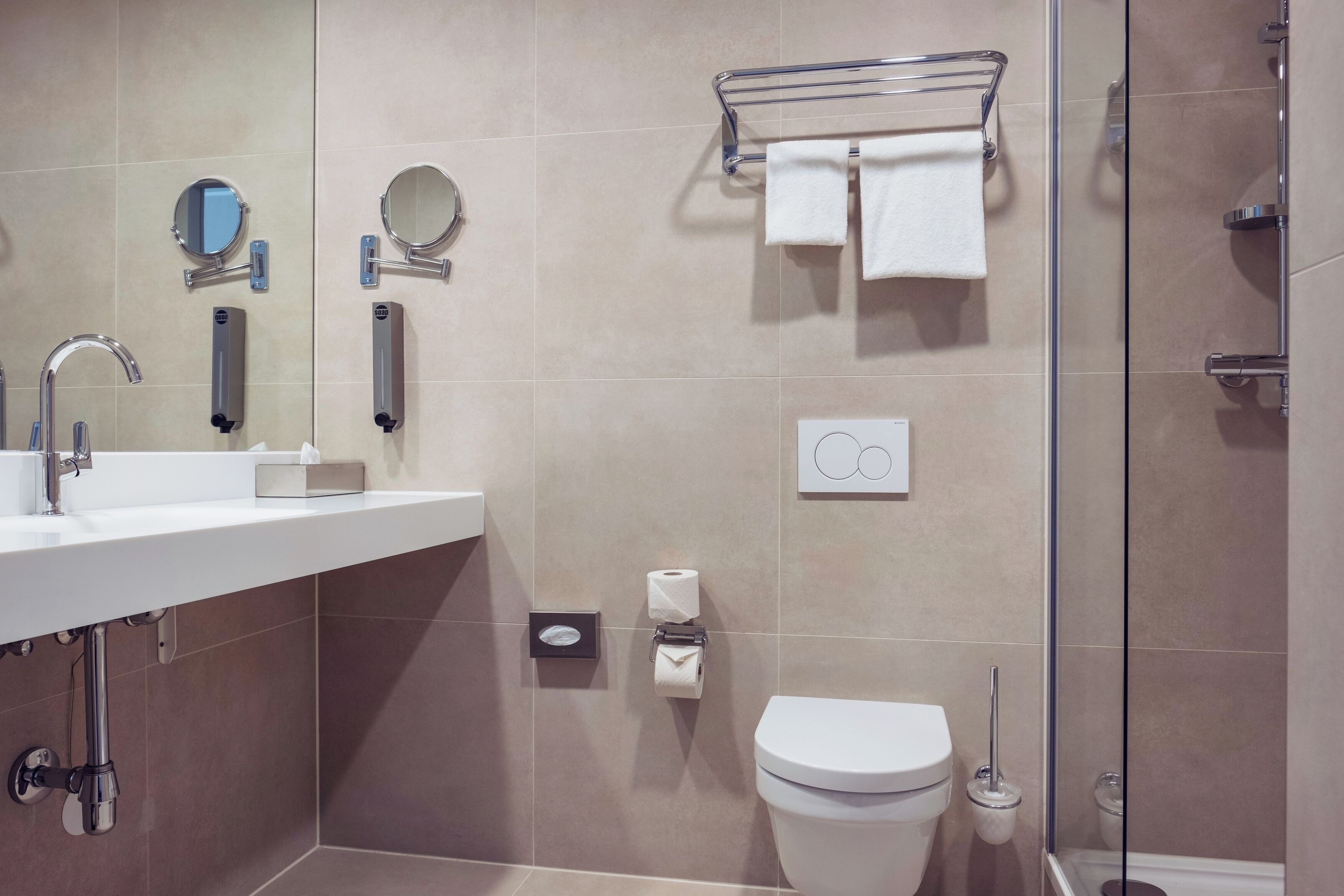 Une salle de bain moderne équipée d’un lavabo, d’un miroir, d’un porte-serviettes, de toilettes et d’une douche.