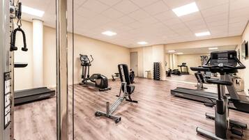 Een sportschool met diverse fitnessapparaten, waaronder loopbanden, een hometrainer en krachtapparaten.