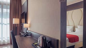 A hotel room with a wooden desk, a telephone, a coffee maker, and a bed with a red blanket.