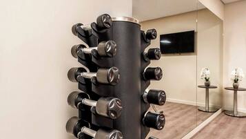 A gym with a wall-mounted dumbbell rack and a flat-screen TV on the wall.