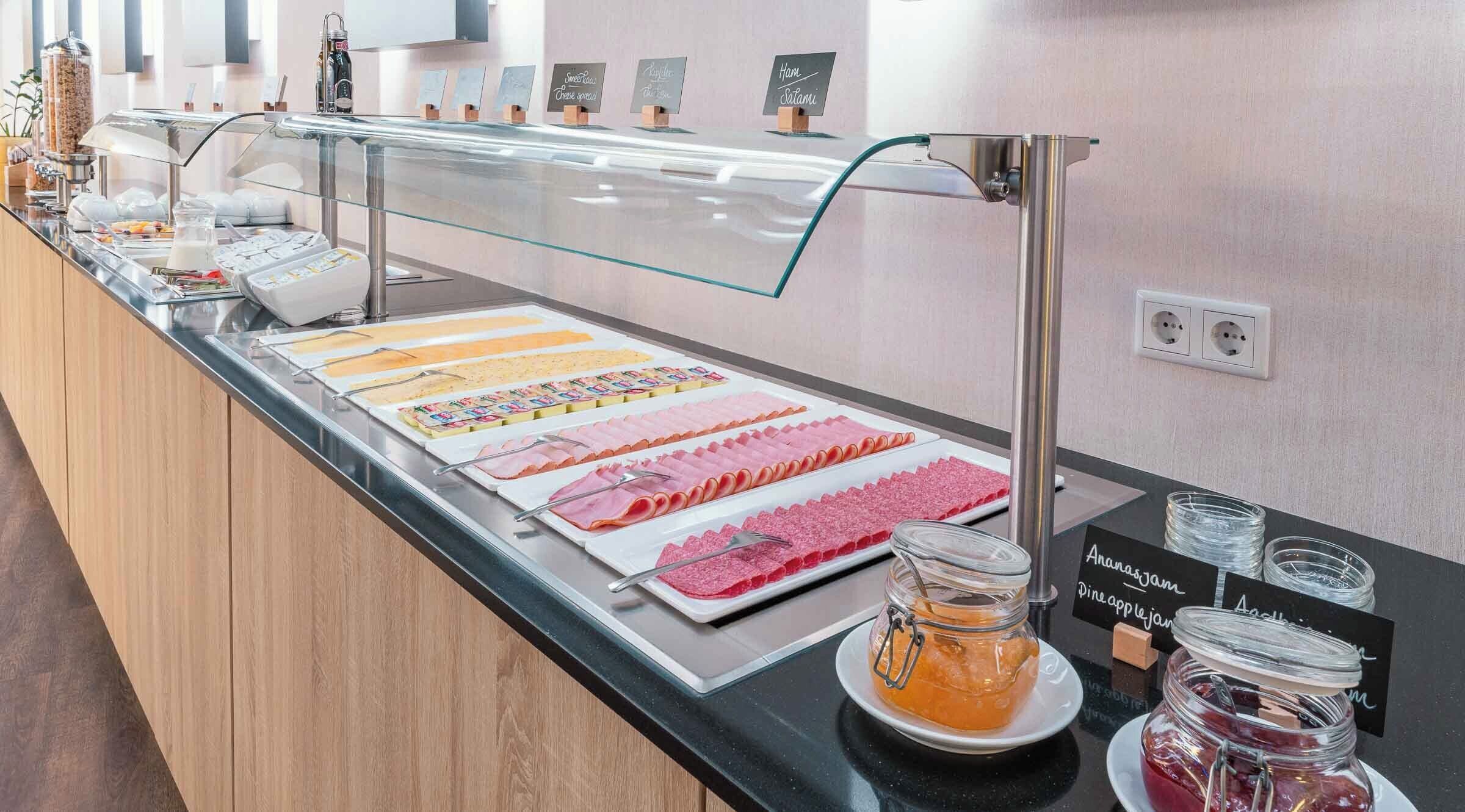 Zona de bufé con diversas opciones de comida, incluyendo embutidos, quesos y un frasco de mermelada de piña.