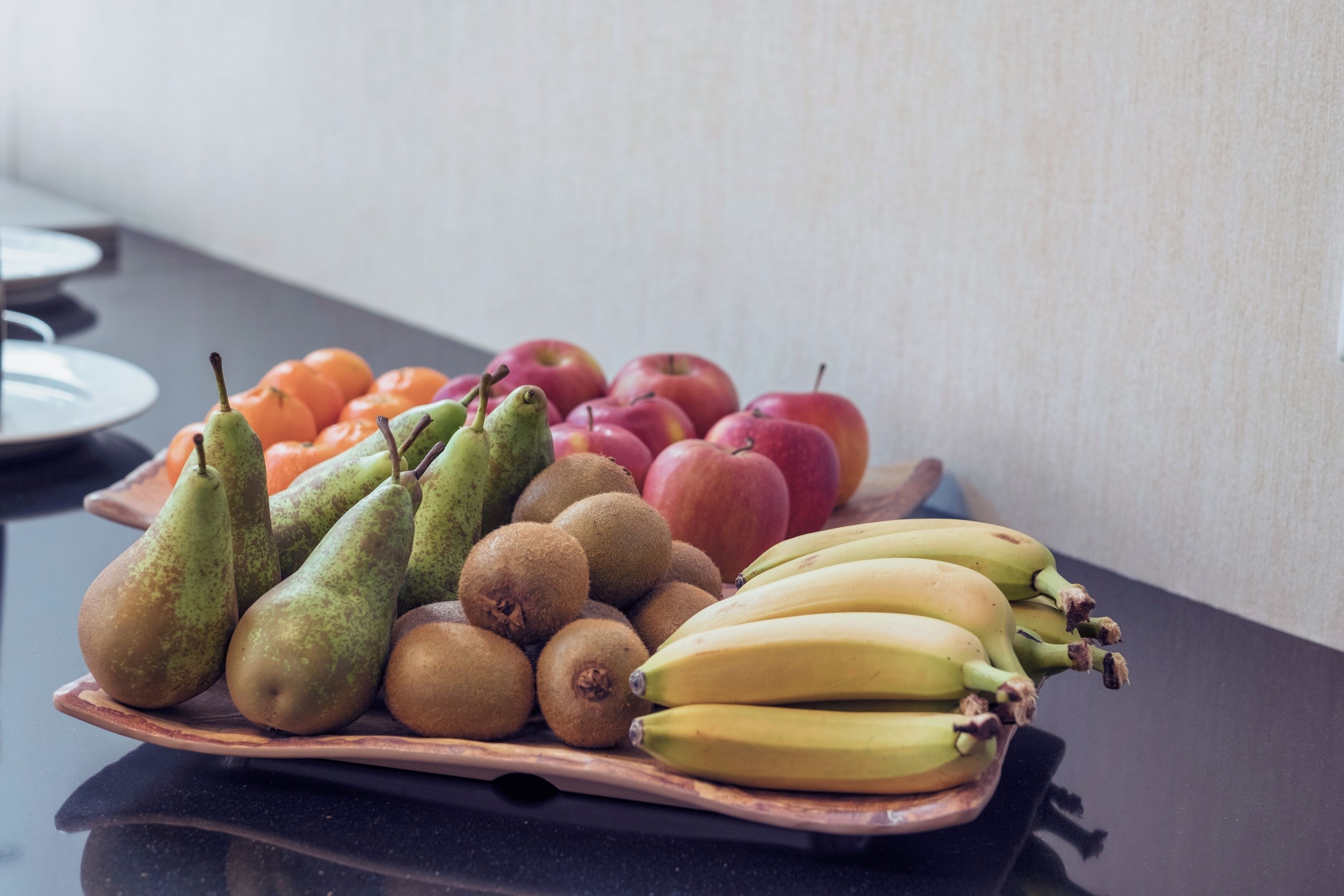 A fruit platter with pears, kiwis, bananas, and apples on a wooden tray.