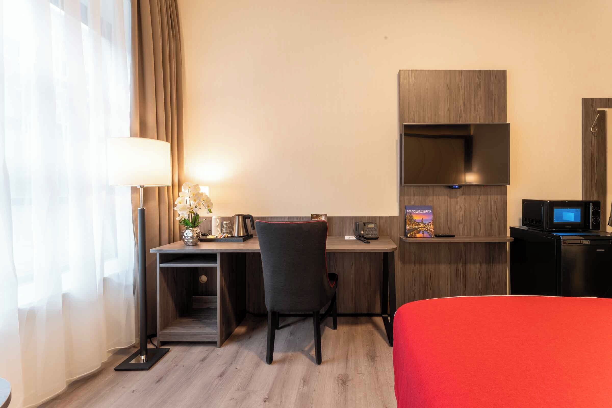 Habitación de hotel con escritorio, silla, cama, televisor y microondas.