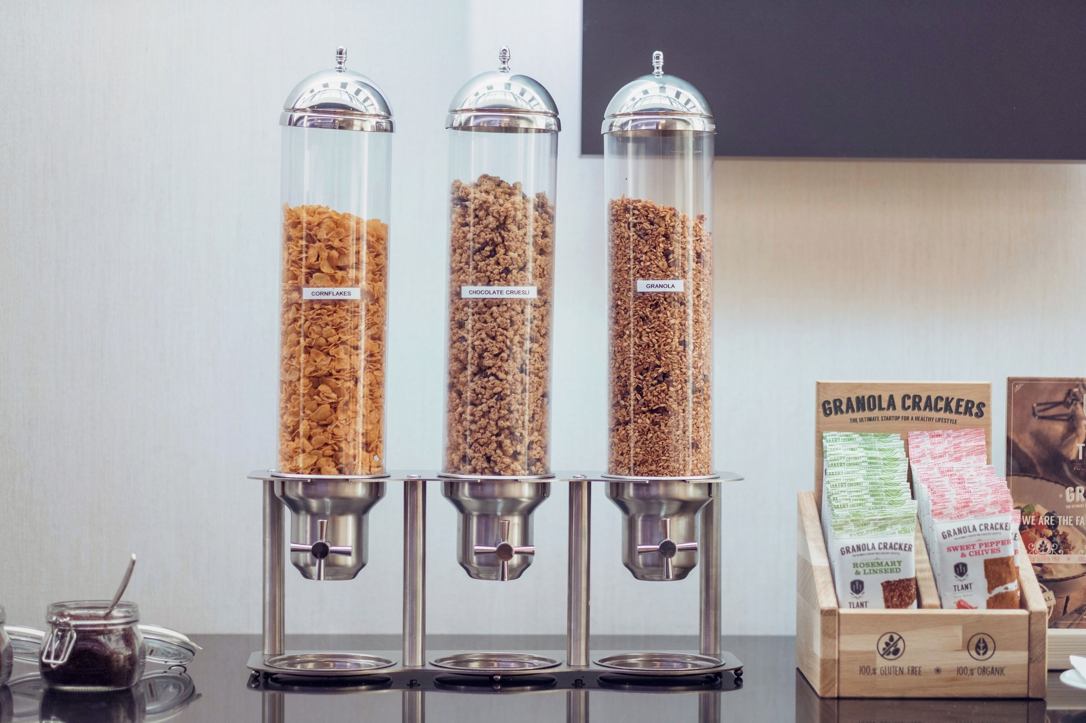 Three glass dispensers with labels for cornflakes, chocolate crumbles, and granola.