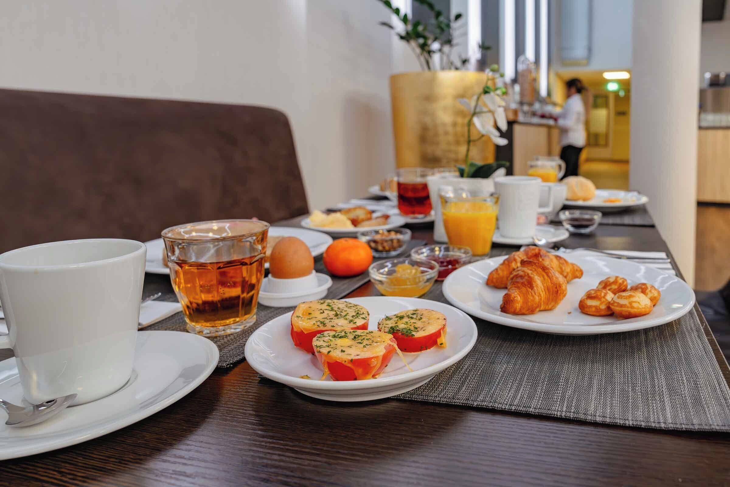 A breakfast setting with croissants, eggs, and juice on a table.