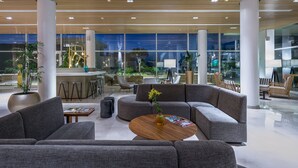 A modern lobby with grey sofas, a wooden coffee table, and a reception desk. - The G Hotel Seashell (El Alamein)