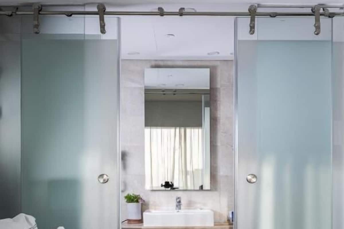 A modern bedroom with a bed, a bathroom with a sink and mirror, and a sliding door.