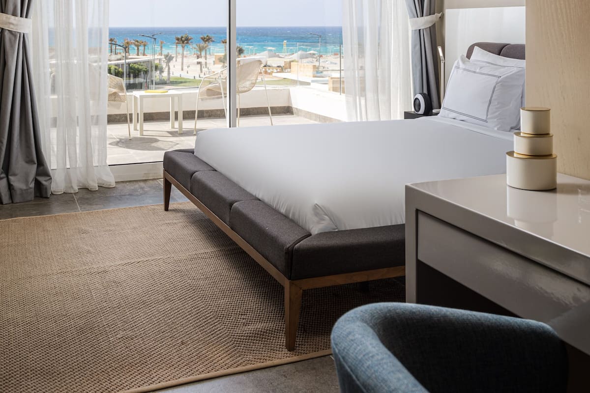 A hotel room with a large bed, a desk, and a view of the beach.