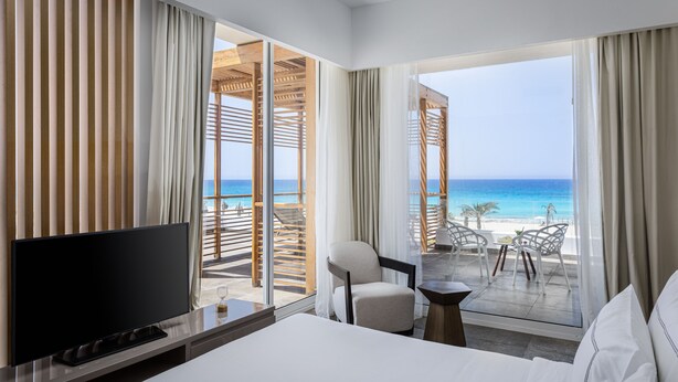 A hotel room with a large bed, a TV, and a balcony with a view of the beach. - The G Hotel Seashell (El Alamein)