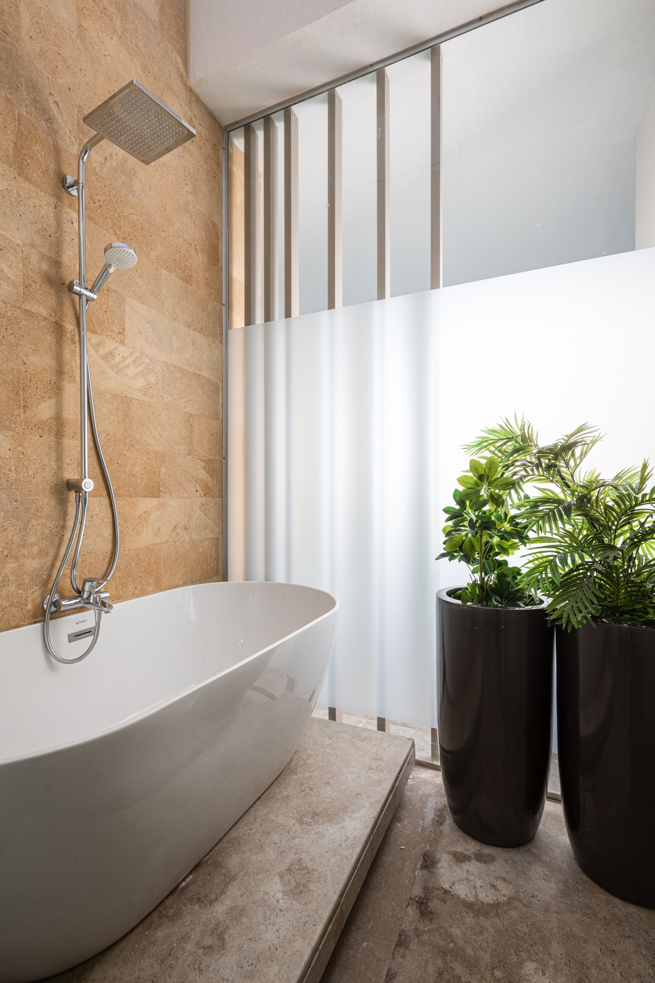 A modern bathroom with a freestanding bathtub, a handheld showerhead, and two potted plants.