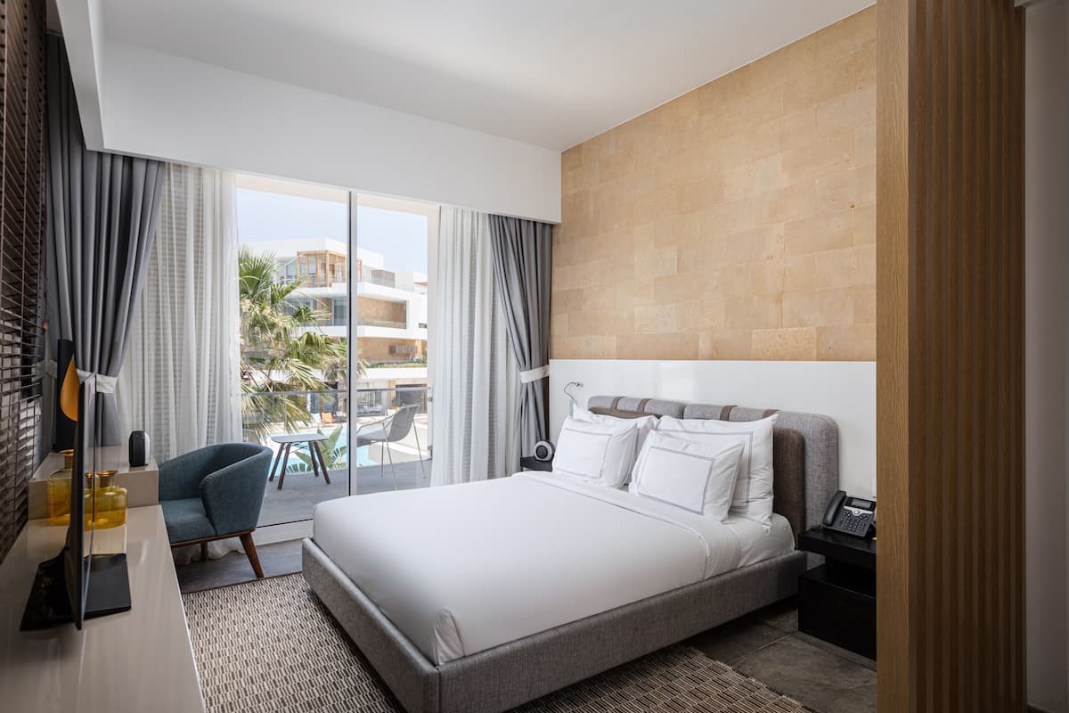 A modern hotel room with a large bed, a desk, a chair, and a view of the outdoors.