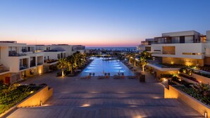A modern hotel with a central pool, multiple balconies, and a view of the sea at dusk. - The G Hotel Seashell (El Alamein)