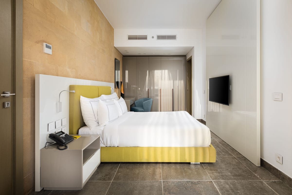 A modern hotel room with a bed, bedside table, and a flat-screen TV mounted on the wall.