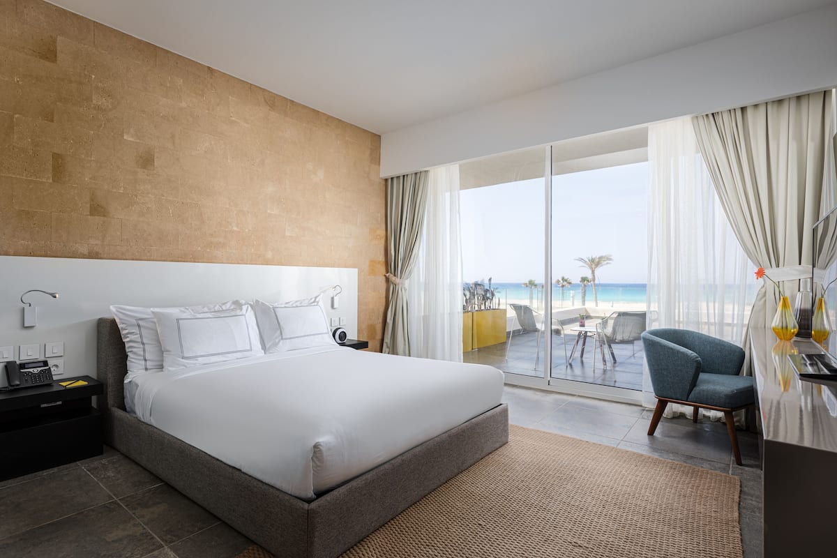 A modern hotel room with a large bed, a desk, and a view of the beach.