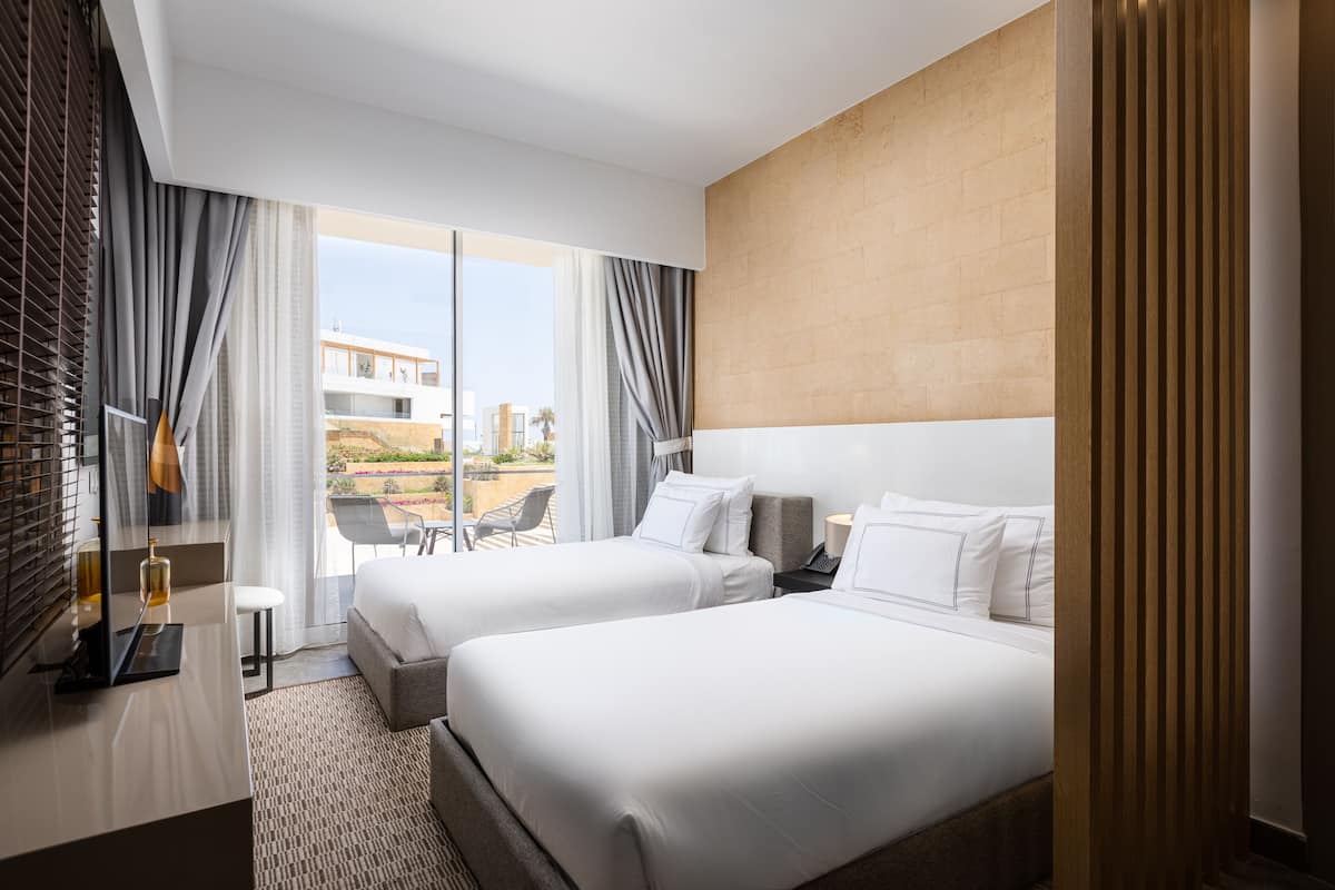 A hotel room with two beds, a desk, and a large window with curtains.