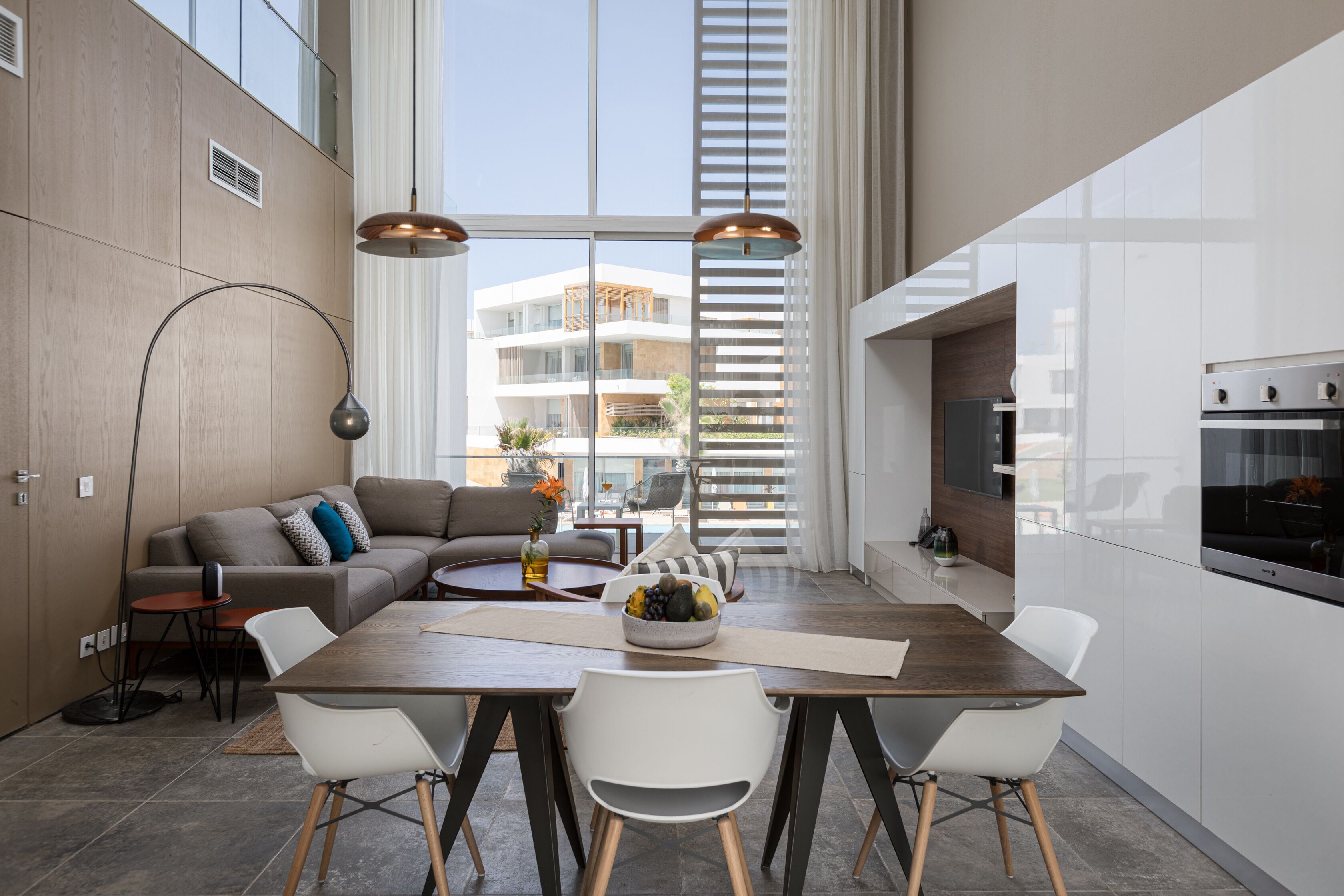 A modern kitchen with a dining area, large windows, and a view of buildings outside.
