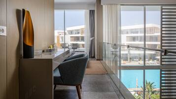 Una habitación de hotel moderna con balcón, zona de comedor y vistas a la piscina y edificios.