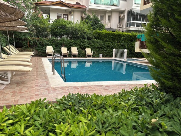 A swimming pool with lounge chairs, a metal ladder, and a hedge in the foreground. - Ustun Apart (Marmaris)