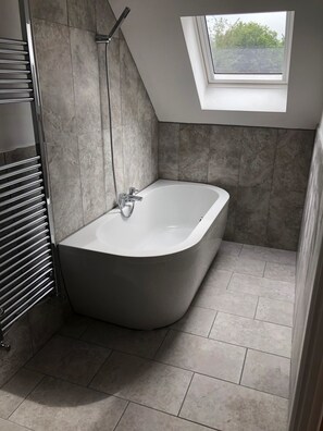 A modern bathroom with a freestanding bathtub, a towel rack, and a skylight. - Hamilton Arms (Midhurst)