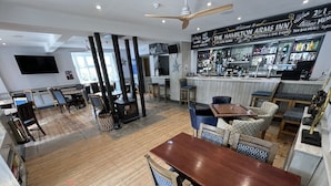 Un restaurante con piso de madera, varias mesas y sillas, una zona de bar y una pantalla de televisión grande.