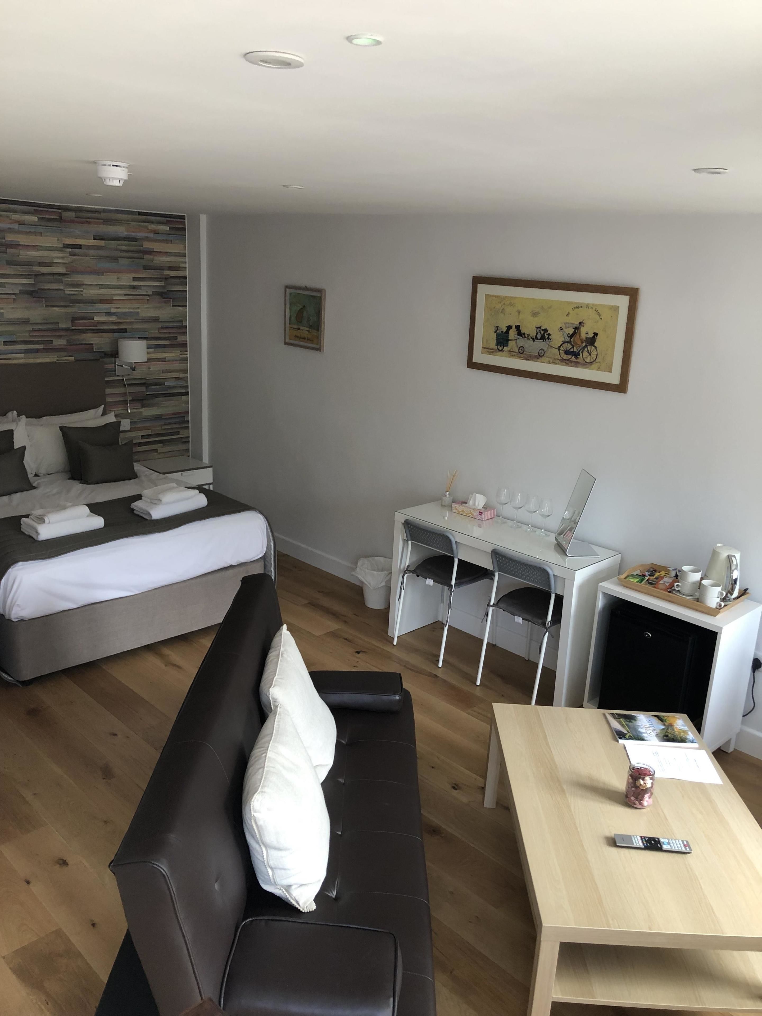 A modern hotel room with a bed, a sofa, a desk, and a dining table.