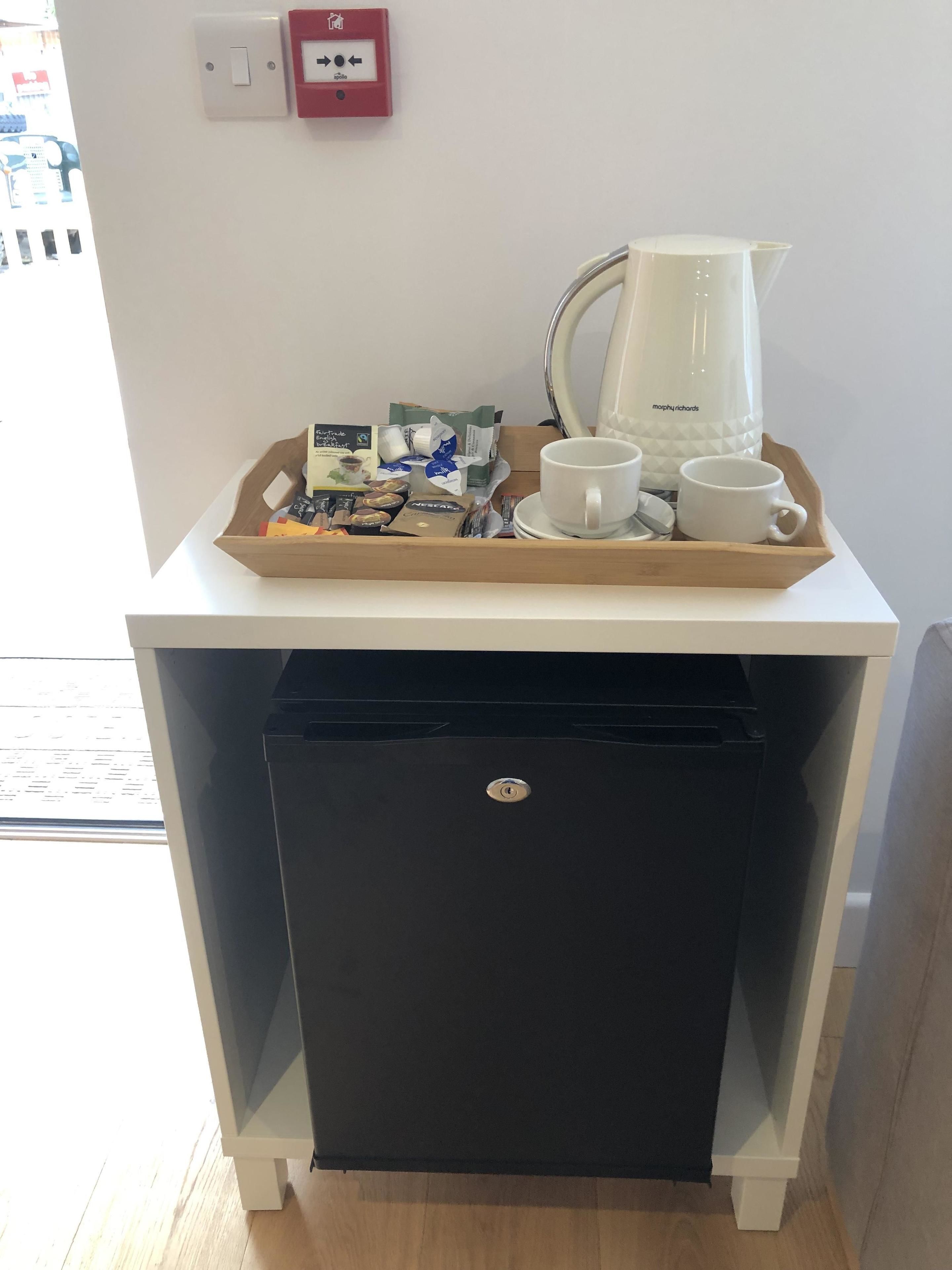 Una kitchenette pequeña con cafetera, tazas y una bandeja de bocadillos.