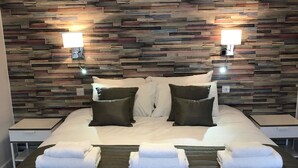 A hotel room with a large bed, two bedside tables, a wooden headboard, and two wall-mounted lights.