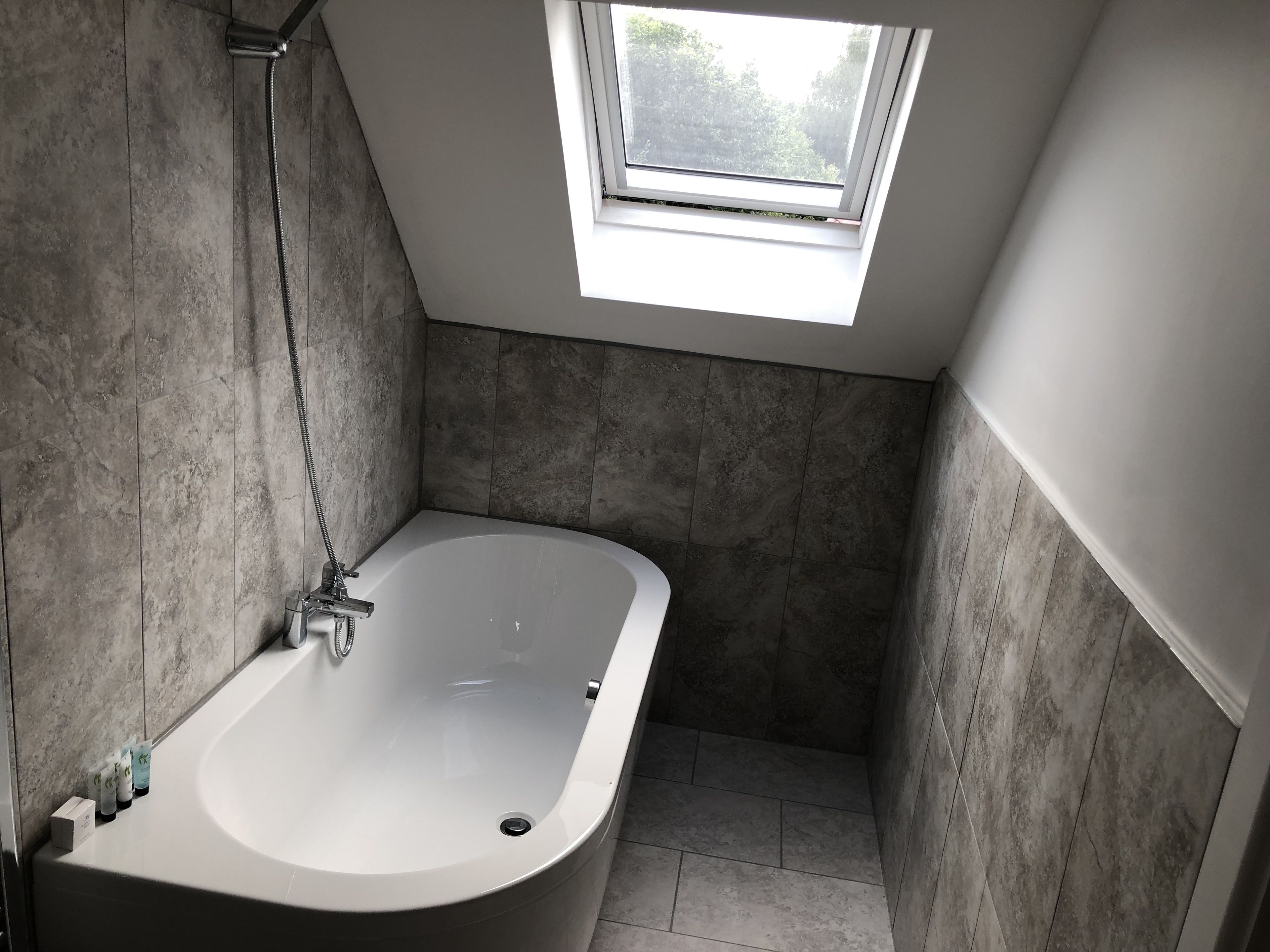 A modern bathroom with a freestanding bathtub, a skylight, and tiled walls.