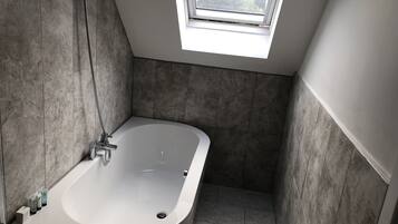 A modern bathroom with a freestanding bathtub, a skylight, and tiled walls.