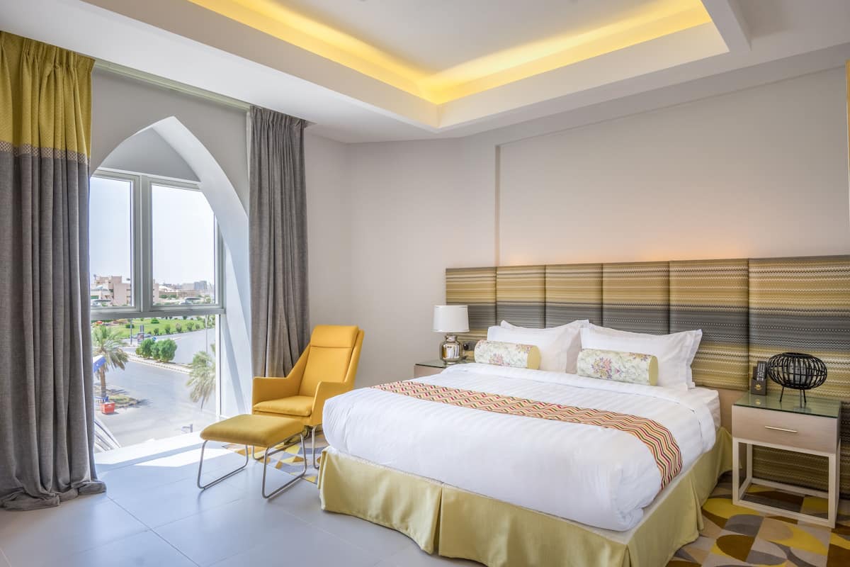 Ein Hotelzimmer mit einem großen Bett, einem Sessel, einem Nachttisch und Blick auf die Stadt.