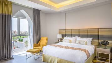 Een hotelkamer met een groot bed, een stoel, een nachtkastje en uitzicht op de stad.