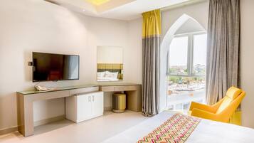 Une chambre d’hôtel moderne dotée d’un grand lit, d’un bureau avec un téléviseur à écran plat, d’une chaise et offrant une vue sur la ville grâce à une grande fenêtre.