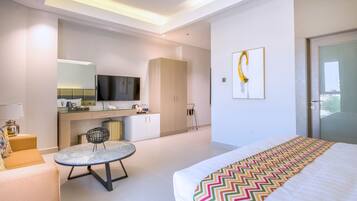 Una habitación de hotel moderna con cama, una pequeña mesa redonda, un sofá, televisor, minibar y un ventanal grande.