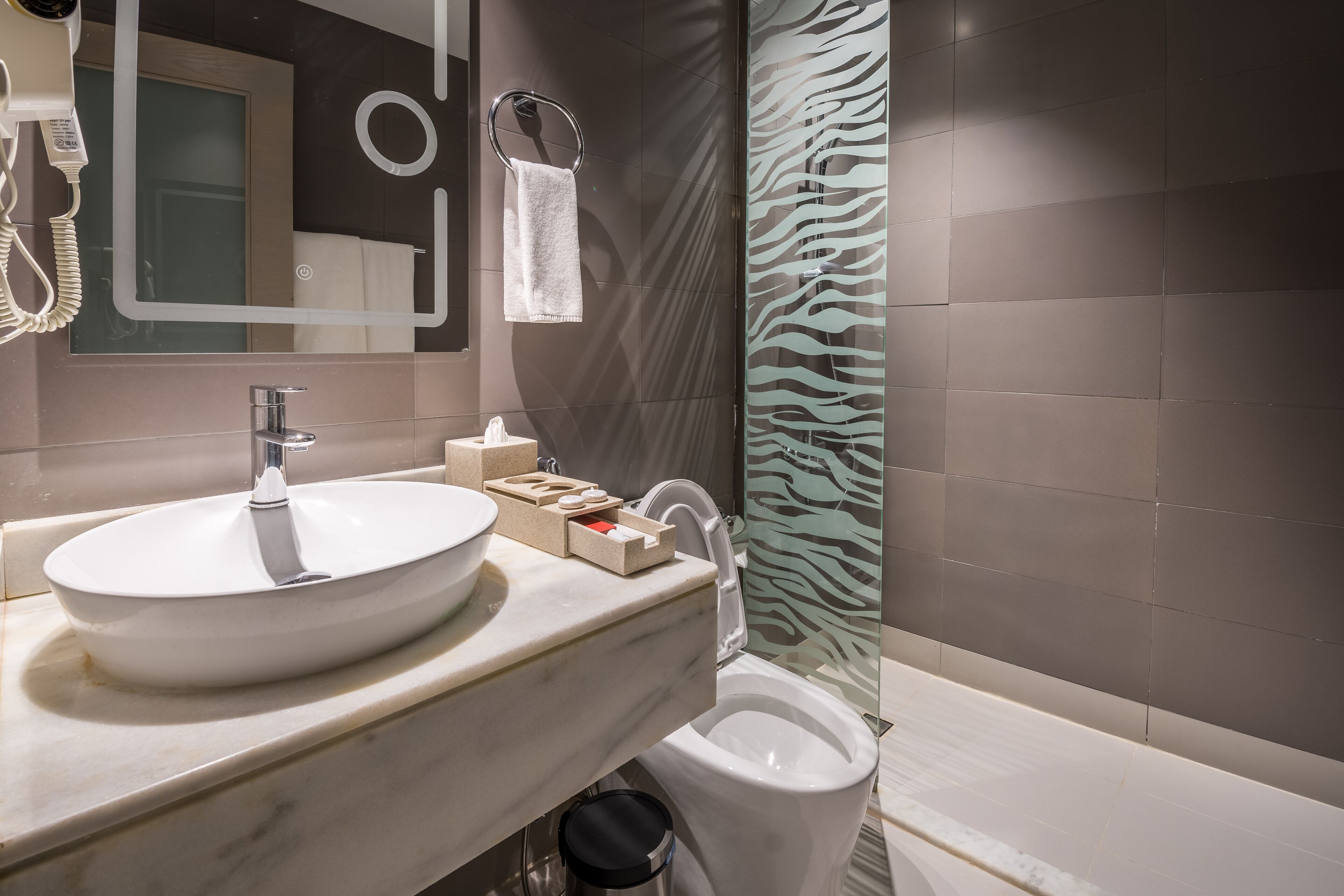 A modern bathroom with a large white sink, a mirror, a towel rack, and a zebra-patterned shower curtain.