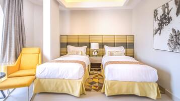 A hotel room with two beds, a yellow armchair, a bedside table with a lamp, and a large abstract painting on the wall.