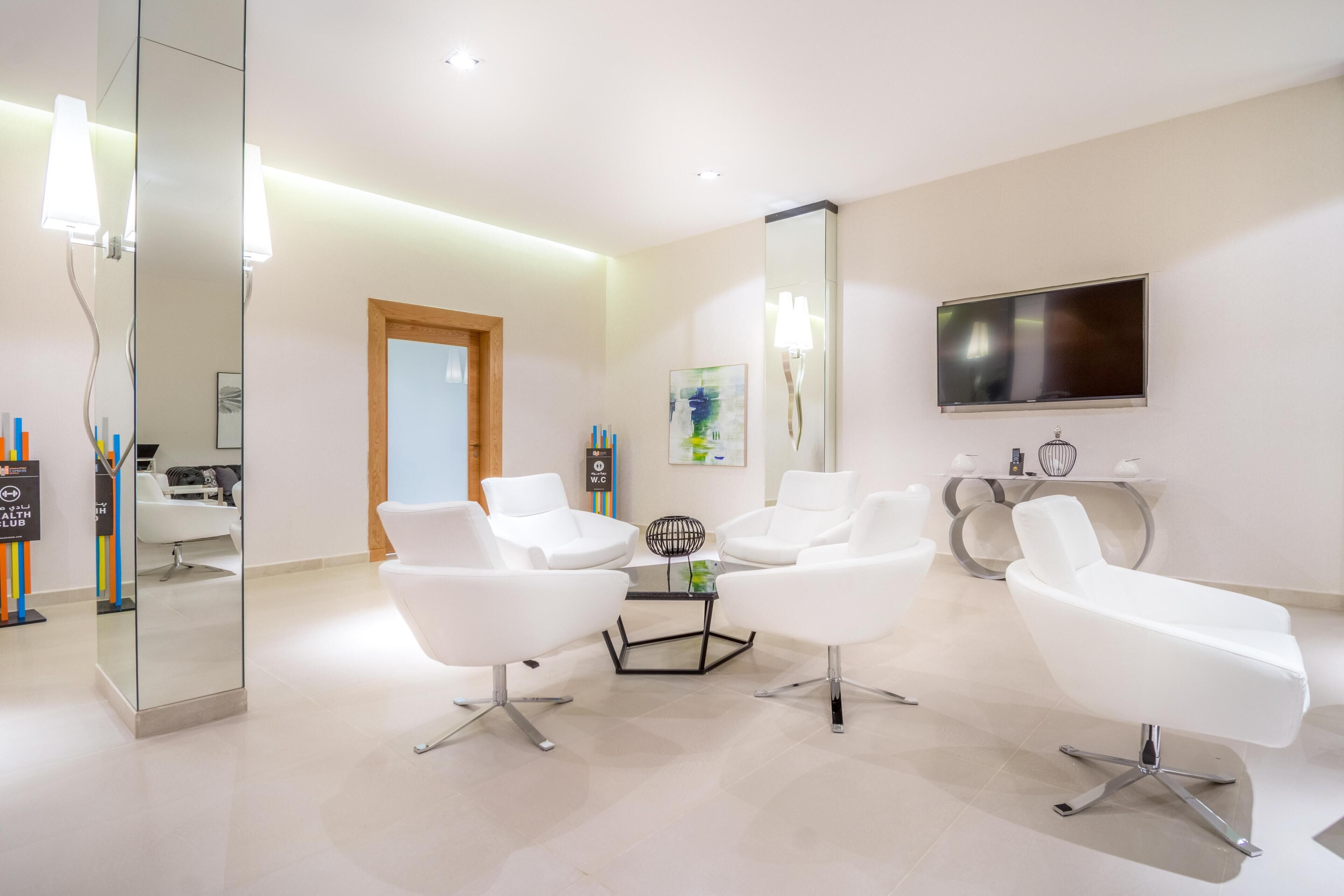 Una habitación moderna y luminosa con muebles blancos, un televisor de pantalla plana y un separador de vidrio.