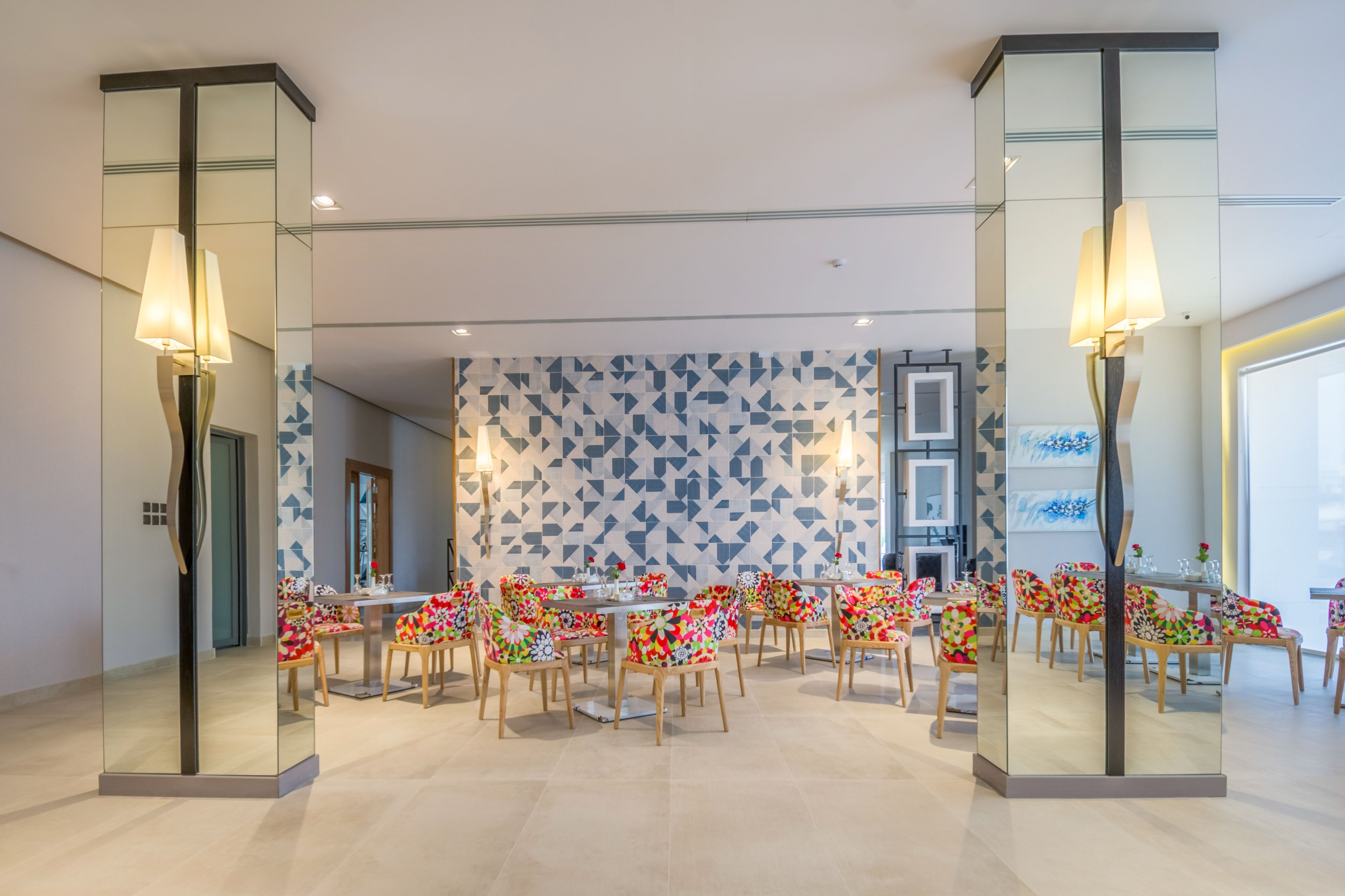 A modern dining area with glass partitions, colorful chairs, and a geometric patterned wall.