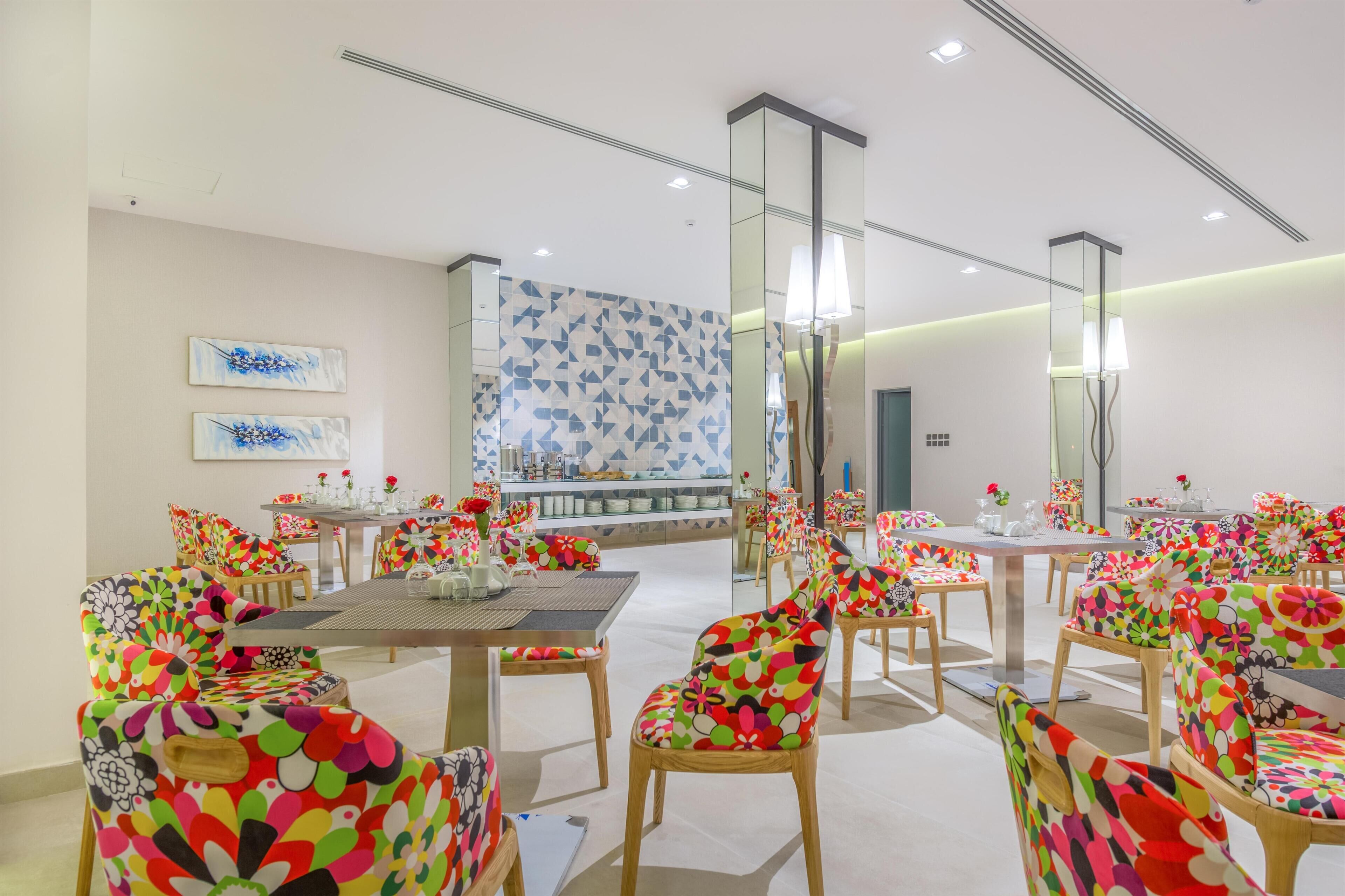 A dining area with colorful chairs and tables, a patterned wall, and a mirror reflecting the room.